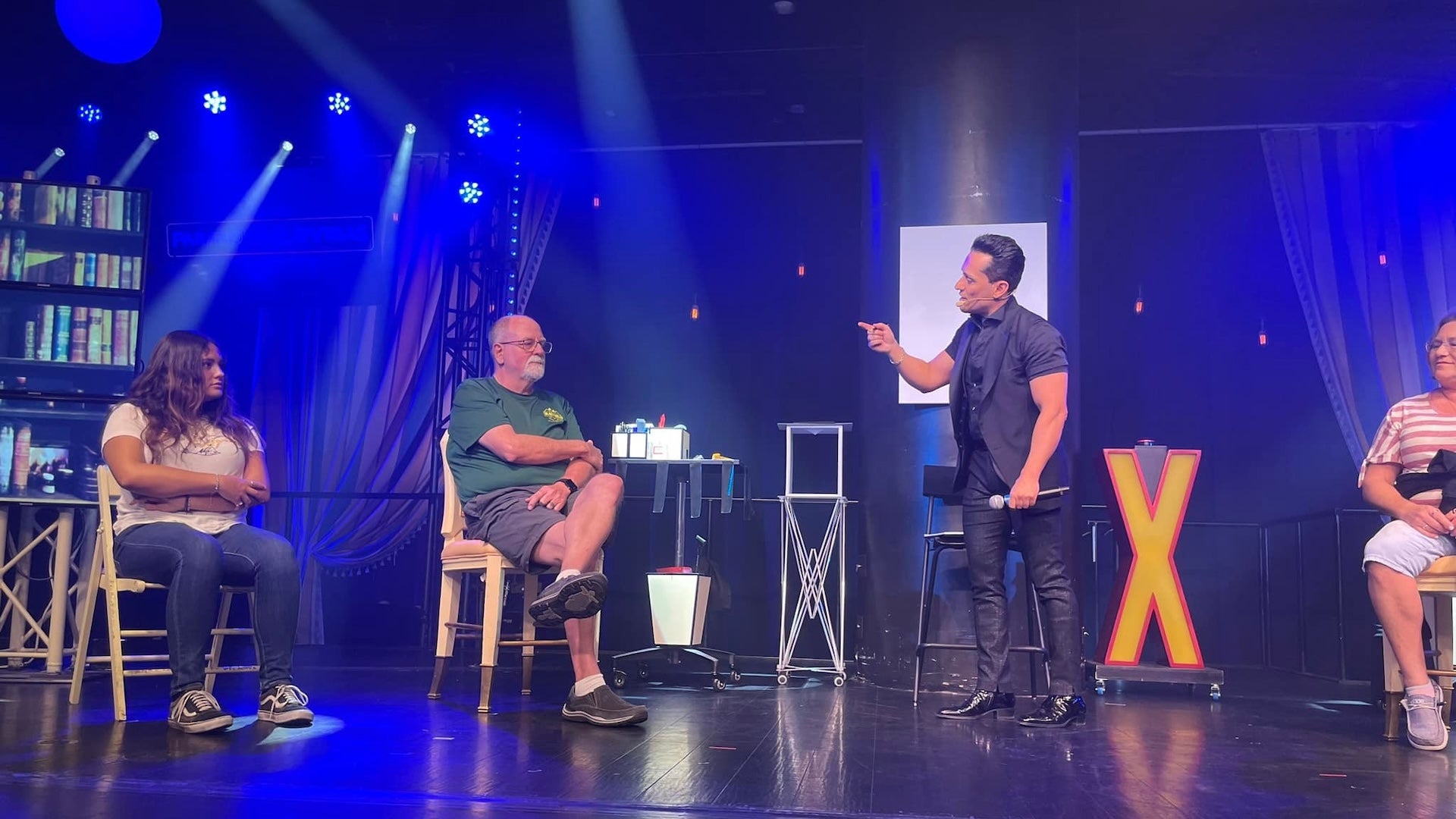 a man standing holding a microphone and three other people sitting